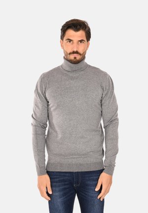 Maglione grigio a collo alto con bordi e polsi a costine, realizzato in un tessuto morbido e liscio. Indossato con jeans blu scuro.