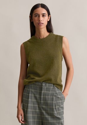 Top sans manches vert olive en tricot doux, associé à un pantalon en laine grise claire à carreaux avec taille haute et poches latérales.