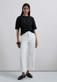Top negro de manga corta con detalles de encaje, combinado con pantalones de pierna ancha blancos y mocasines negros. Tejido suave, corte entallado, diseño minimalista.