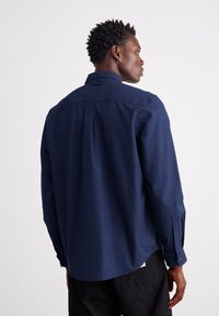 Camicia a maniche lunghe blu navy in cotone, con colletto a punta, polsini abbottonati e orlo curvo. Design semplice e pulito.