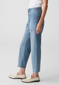 Jeans in denim azzurro chiaro con una vestibilità rilassata, dotati di tasche anteriori e posteriori e orlo risvoltato. Il tessuto ha una texture liscia.
