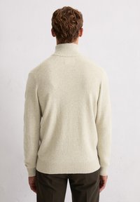 Jasno beżowy sweter z wysokim kołnierzem, z prążkowanymi mankietami i dolnym wykończeniem. Wykonany z teksturowanej tkaniny, charakteryzujący się lekko luźnym krojem i minimalistycznym designem.