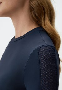 Marineblaue Kleidung mit einem glatten Stoffkörper, strukturierten Netzärmeln, rundem Ausschnitt und weichem Finish insgesamt.