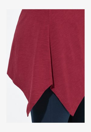 Bordeaux top met een afgeronde zoom en spitse randen, gemaakt van een zachte, gestructureerde stof, gecombineerd met donkerblauwe broek in de afbeelding.