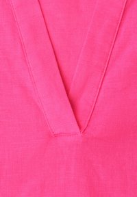 Tissu rose vif avec un col en V et des coutures visibles le long des bords.