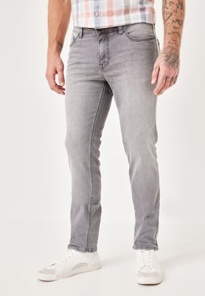 Gray denim jeans with a slim fit and visible stitching details. Worn with white sneakers, showcasing a casual, contemporary look.