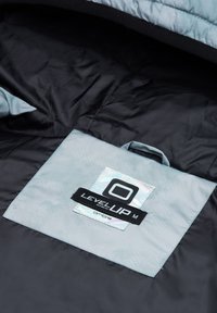 Interiér spacáku s světle modrou úložnou taškou označenou "LEVEL UP M ombre" na černém textilním pozadí.