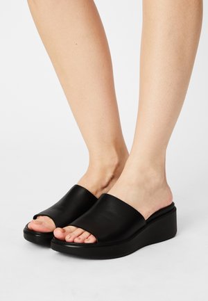 Sandales à semelle compensée en cuir noir avec un design à bout ouvert et une texture lisse. La semelle est épaisse et légèrement courbée pour un confort optimal.
