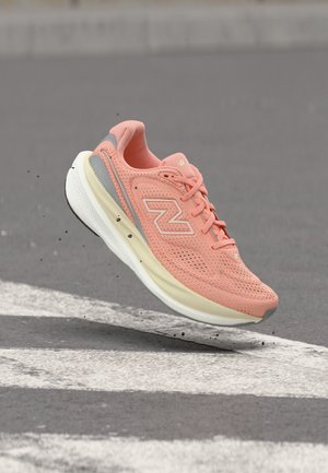 Zapatilla de running New Balance de color rosa claro con suela blanca capturada en el aire sobre una superficie de asfalto gris con marcas viales blancas.