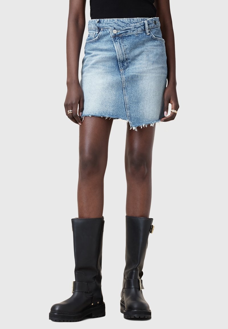 Vue de face d'une personne portant une mini-jupe en denim bleu clair à ourlet brut et des bottes noires montantes à boucles.