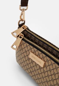 Borsa marrone a fantasia con cerniere e accessori dorati, caratterizzata da un design geometrico. Un'etichetta metallica riporta la scritta "RIVER ISLAND" su un lato.