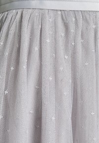 Tessuto di tulle grigio chiaro con piccoli motivi floreali ricamati, arricciato in vita con un nastro di raso liscio. Texture morbida e trasparente.