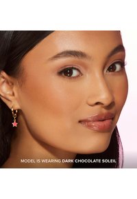 Gouden hoepeloorbel met een roze sterrenbedeltje, met een gladde afwerking, gedragen door een model met een natuurlijke make-up look en glanzende lippen.