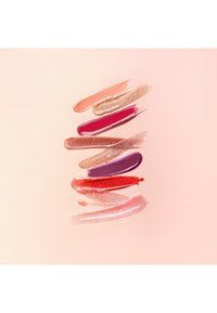 Sieben horizontale Lipgloss-Farbmuster in Pfirsich-, Goldschimmer-, Pink-, Nude-Schimmer-, Violett-, Rot- und Hellrosa-Tönen auf einem blasspfirsichfarbenen Hintergrund.