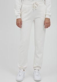 Cremefarbene Sweatpants aus weichem Stoff, mit einem elastischen Bund und Kordelzug, gerippten Knöcheln und seitlichen Taschen.