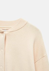 Cardigan en tricot beige clair avec col rond et boutons-pression, montrant les détails du haut devant et des épaules.