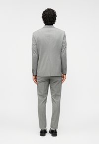 Γκρι κοστούμι, υφασμάτινη υφή, εφαρμοστό σχέδιο, ραμμένο σακάκι, ίσια παντελόνια και μαύρα παπούτσια. Βλέπεται από πίσω.