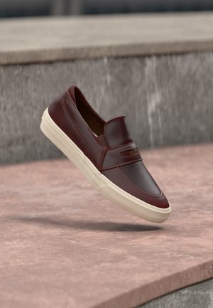 Brown leather slip-on sneaker with white rubber sole floating above stone surface against gray stone background.
