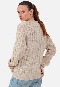Pull beige en maille présentant un motif texturé, des manches amples et un ourlet côtelé. Style décontracté, idéal pour le superposition.