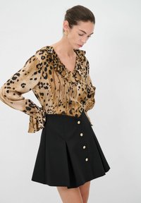 Blusa con stampa leopardata, con scollo e polsini arricciati, abbinata a una gonna plissettata nera con bottoni dorati.