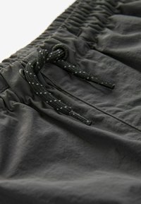 Shorts noirs avec une taille élastique, dotés d'un cordon de serrage texturé avec des embouts en plastique et de légères plis dans le tissu pour plus de détails.