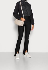 Czarna krótka kurtka z elastycznym dołem, czarne spodnie z wysokim stanem i bocznymi rozcięciami oraz beżowa torebka na ramię. Białe trampki dopełniają outfit.