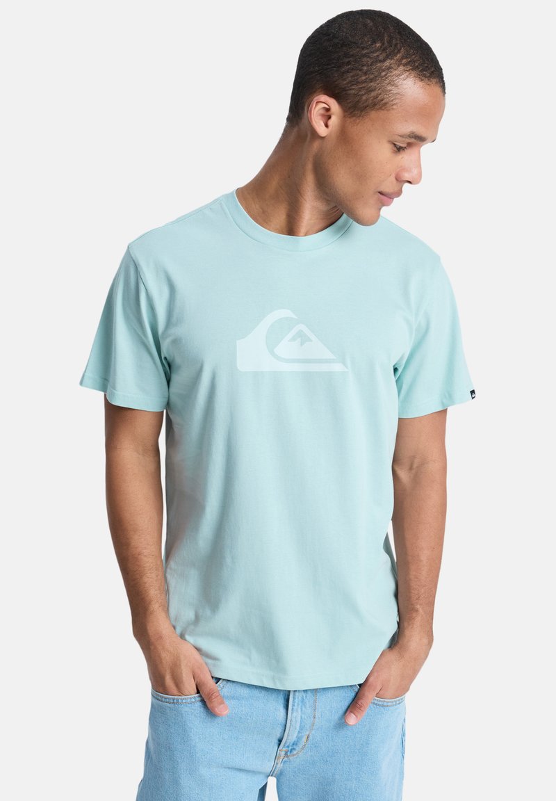 Γαλάζιο βαμβακερό t-shirt με στρογγυλή λαιμόκοψη και κοντά μανίκια. Διαθέτει λευκό λογότυπο στην μπροστινή πλευρά. Φορεμένο με τζιν σορτς.