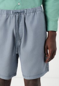 Pantalones cortos grises de tejido con cintura elástica y cordón. Cuenta con bolsillos laterales y un ajuste relajado. Textura suave, sin patrones.