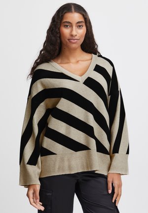Pull beige avec de larges rayures diagonales noires, col en V, coupe ample, ourlet et poignets côtelés, texture douce et silhouette décontractée.