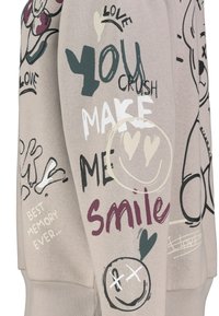 Light beige sweatshirt with various graphic prints including text and doodles in colors like black, green, and maroon, with ribbed cuffs.