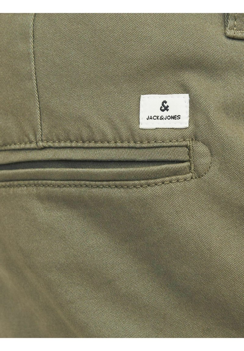 Tela de algodón verde oliva con un bolsillo con cremallera y una etiqueta blanca con texto negro que dice "JACK & JONES." Textura suave con detalles de costura.