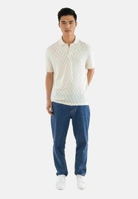 Hvit kortermet polo skjorte med diamantmønster, kombinert med blå jeans og hvite sneakers. Skjorten har klassisk krage og avslappet passform.