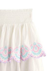 Gonna bianca in cotone con una vita arricciata e un orlo scallopato, decorata con motivi in ricami nei toni pastello di rosa e azzurro. Tessuto morbido e strutturato.