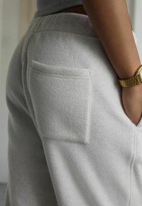 Suure plaan isikust, kes kannab heledat halli fliispükse, millel on tagakott, käsi küljekotis ja vasakus randmes kuldne käekell.