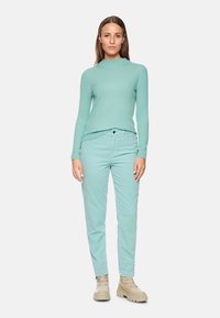 Mintgrünes, geripptes Langarmoberteil, kombiniert mit passenden mintgrünen Slim-Fit-Hosen und beigen klobigen Stiefeln. Schlichtes, modernes Design.