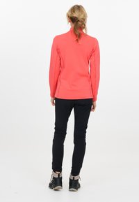 Korallenfarbene Langarmbluse mit hohem Kragen, strukturiertem Stoff, kombiniert mit schwarzen Slim-Fit-Hosen und schwarzen Wanderschuhen.