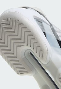Gros plan de la semelle blanche d'une basket montrant un motif de bande de roulement en zigzag et une partie du côté de la chaussure avec un détail en mesh et une bride.