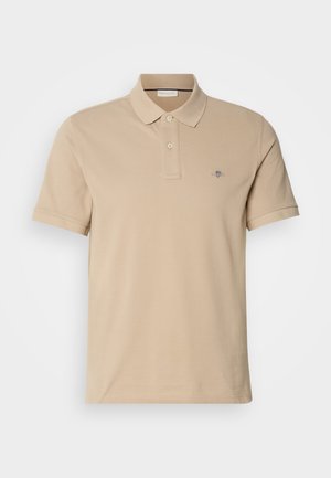 Beige polo shirt made from cotton, featuring a buttoned collar, short sleeves, and a small embroidered logo on the chest. Smooth texture.