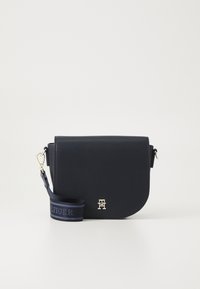 Námořnická křížová taška z umělé kůže s zakřiveným klopou, zlatým logem a odnímatelným popruhem s modrou texturovanou štítkem.