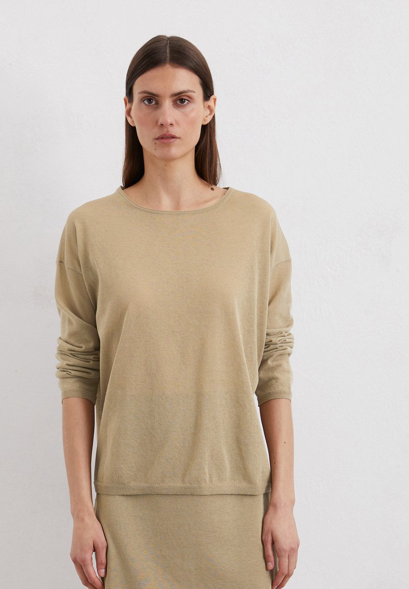 Haut beige à manches longues en tissu doux, avec une coupe décontractée. Il présente un col rond et des épaules tombantes, avec des poignets et un ourlet côtelés.