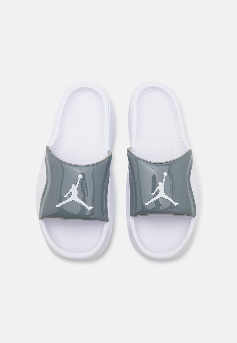 Riemensandalen mit einem glänzenden grauen Riemen, der ein weißes Jumpman-Logo zeigt, auf einem strukturierten weißen Fußbett mit ausgeprägten Rillen für besseren Halt.