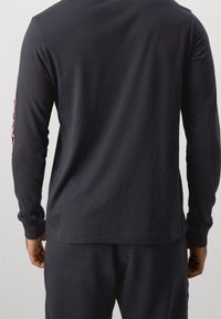 Dunkelblaues Langarmshirt mit glatter Textur, das pinke Grafikdesigns an den Ärmeln aufweist. Einfacher, lässiger Schnitt mit Rundhalsausschnitt.