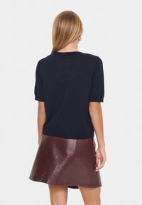 Haut en maille bleu marine à manches courtes associé à une jupe trapèze en cuir bordeaux. La tenue présente un col rond et un détail de bord côte.