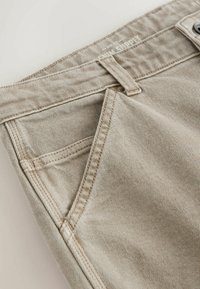 Beige denim trousers featuring a straight cut, front pockets, subtle vertical stripes, and contrasting stitching. One button closure at the waist.