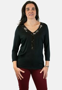 Top negro de manga larga con escote en V, que presenta un diseño decorativo de lentejuelas a lo largo del escote. Combinado con pantalones burdeos.