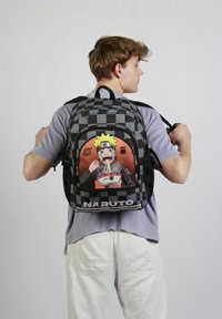 Sac à dos à carreaux noir et gris avec un graphique de Naruto au dos, mettant en avant des couleurs vives, un design de personnage détaillé et le texte "NARUTO."