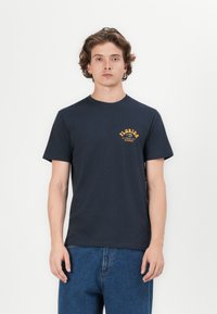 Navy cotton t-shirt with short sleeves, featuring an orange graphic logo on the left chest and a crew neckline.