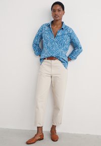 Blå mönstrad skjorta med vitt blommönster, beige byxor och bruna vävda skor. Skjortan har knappslå och långa ärmar.