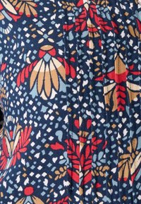 Tessuto blu navy con un motivo floreale che presenta accenti rossi e dorati, dettagli azzurri chiari e piccoli cuori bianchi. Texture plissettata visibile.