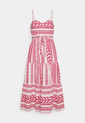 Robe blanche sans manches avec des motifs géométriques et tribaux rouges, bretelles spaghetti et ceinture nouée à la taille.